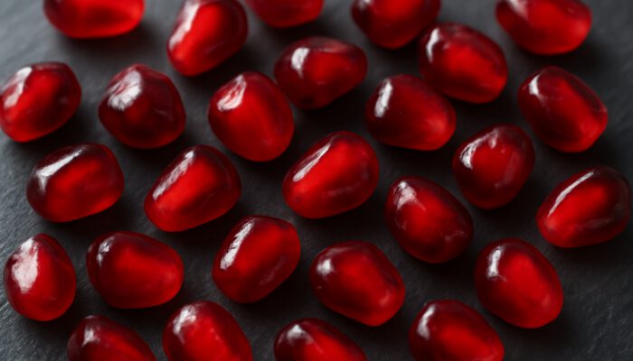 Plump red and purple pomegranate seeds scattered on dark slate surface