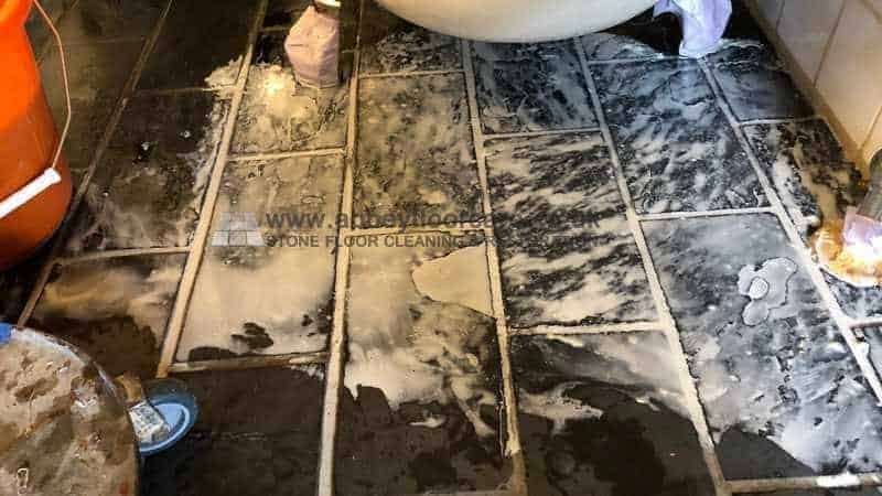 Riven slate floor with dark edges and uneven old coating before stripping